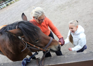 Dziewczynka wraz z terapeutą podczas karmienia konia marchewką.
