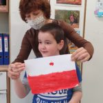 Chłopiec wraz z nauczycielem trzymający flagę Polski.