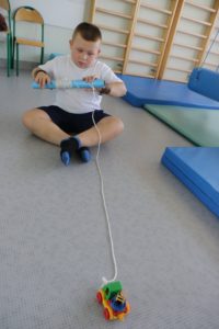 Uczeń podczas aktywności rozwijającej koorydnację obustronną rąk - nawijanie sznurka na rolkę.