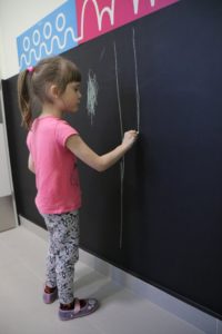 Dziewczynka rysująca kredą linie pionowe na tablicy ściennej.