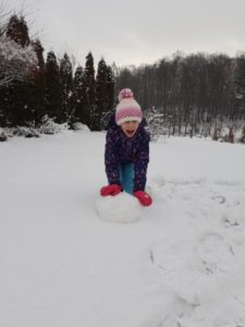 Dziewczynka lepiąca "kulę" na śniegowego bałwanka.