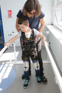Uczeń w kominezonie Dunag podczas ćwiczeń z fizjoteraputą na poręczach asekuracyjnych.