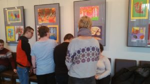 Grupa uczniów obserwująca prezentowane w fotoramach prace plastyczne podczas wystawy "Jesienne wspomnienia".