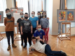 Zdjęcie grupy uczniów na tle wystawy prac plastycznych podczas wystawy "Jesienne oblicza".