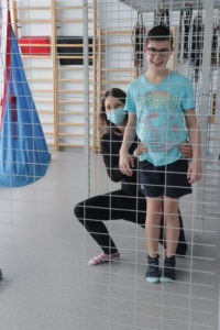 Uczeń wraz z terapeutą podczas ćwiczeń koercji wad postawy przez lustrem.