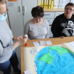 Uczniowei wraz z wychowawcą podzcas oklejania pracy plastycznej "Planeta Ziemia" tematycznymi symbolimi MAKATON.