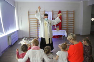 Ksiądz podczas błogosławieństwa wielkanocnych pokarmnów prezentujący przedszkolakom chleb.