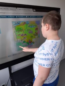 Uczeń układający puzzle mapy polski na tablicy interaktywnej.