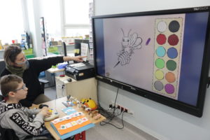Uczeń wraz z teraputą podczas pracy na tablicy interaktywnej z wykorzystaniem dostosowanej do potrzeb niepełnosprawnych ruchowo osób specjalistycznej "myszki:.