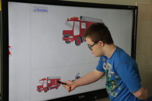 Uczeń podczas pracy dopasowywania identycznego zdjęcia pojazdu straży pożarnej na tablicy interaktywnej.