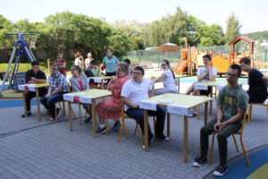 Absolwenci siędzący przy "egzaminacyjnych" stołach na szkonym podwórku.