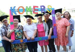 Uczniowie wraz z nauczycielem pozujący w kolorowej ramce z napisem Komers.