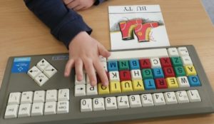 Fragment dłoni ucznia podczas pracy na specjalistycznej klawiaturze piszącej słowo BUTY.