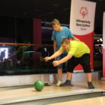 Uczestnik turnieju wraz z asystą w trakcie rzutu kulą bowlingową.