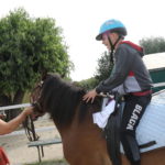 Uczeń podzcas jazdy na koniu w trakcie zajęć hipoterapii, z indywidualnym tematycznym komunikatorem AAC z wykorzystaniem symboli MAKATON>