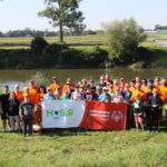 Uczestnicy Regionalnego Spływu Rzeką Odrą podczas grupowego zdjęcia na tle rzeki Odry z banerem OSS i MOSiR Rybnik.