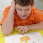 Uczeń podczas układania puzzli ilustracji dyni z napisem Dzień Dyni.