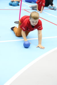 Młody sportowiec podczas aktywności toczenia piłki w pozycji czworaczej.
