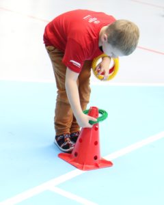 Młody sportowiec podczas aktywności nakładania kółka na pachołek.