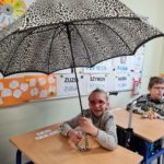Uczennica pozująca z parasolem podczas jesiennych zajęć edukacyjnych.
