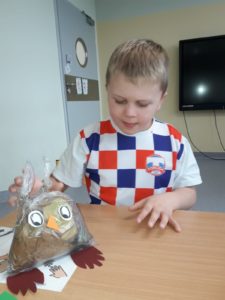 Przedszkolak pozujący z wykonaną przez siebie figurką sowy.