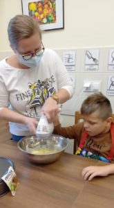 Uczeń podzcas czynności miksowania składników na ciasto z pomocą wychowawcy.