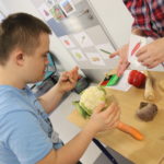 Uczeń przy stole pełnym różnych jesiennych warzyw podczas wyboru zadanego warzywa.