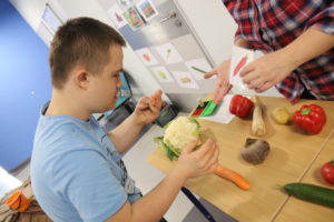 Uczeń przy stole pełnym różnych jesiennych warzyw podczas wyboru zadanego warzywa.