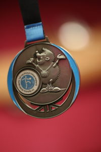 Medal RyBoTuDI 2021 z wizerunkiemmaskotki OS - jeżyka z medalem oraz nazwą i logotypem bolwingu.