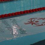 Flaga OSŚ na tafli wody basenu w trakcie Ceremonii Otwarcia zawodów.