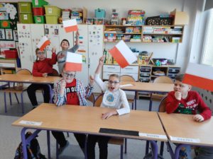 Uczniowie pozujący z wykonanymi przez siebie flagami polski.