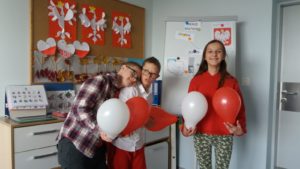 Uczniowie pozujący z biało -czerwonymi balonami, w tle wystwa prac plastycznych "orzełki".