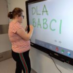 Uczennica pisząca po śladzie napis "dla babci" na tablicy interaktywnej.