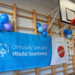 Baner z logo Programu Młodzi Sportowcy OS oraz logotypem partnera programu firmy MATEL zawieszony na drabinkach sali gimnastycznej.