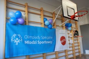 Baner z logo Programu Młodzi Sportowcy OS oraz logotypem partnera programu firmy MATEL zawieszony na drabinkach sali gimnastycznej.