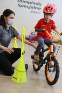Młody Sportowiec podczas nakłądania obręczy na pachołek podczas jazdy na czterokołowym rowerze.