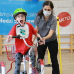 Młody Sportowiec podczas jazdy na trójkołowym rowerze z asekuracją trenera.