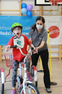 Młody Sportowiec podczas jazdy na trójkołowym rowerze z asekuracją trenera.