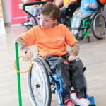 Uczeń na wózku inwalidzkim podczas konkurencji nakładania obręczy na stojak.