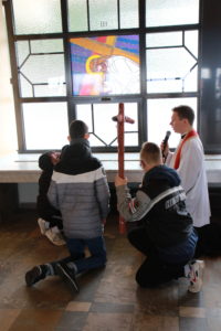 Uczniowei niosący krzyż wraz z księdzem przyklękający przez III stacją Drogi Krzyżowej.