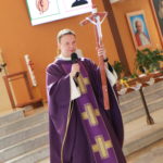 Ksiądz prezentujący wykonany przez uczniów krzyż.