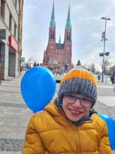 Uczeń podzcas "niebieskiego spaceru pozujący z niebieskim balonem na tle bazyliki.