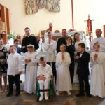Zdjęcie grupowe uczniów przystępujących do I Komunii Św. wraz z księżmi, katechetami na tle ołtarza.
