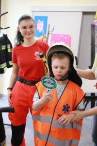 Przedszkolak pozujący w stroju ratownika, z kaskiem strażaka w asyście pani ratownik.