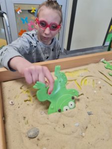 Uczennica podczas aktywności zabawy żabkami i piaskiem.