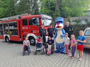 Ekipa podopiecznych pozująca z maskotką Sznupką, strażacki OSP na tle wozu strażackiego.