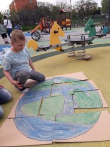Przedszkolak układający duże puzzle z wizerunkiem kuli ziemskiej.