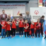 Młodzi Sportowcy wraz z trenerami pozujący z medalami.