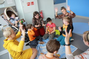 Przedszkolaki wraz z wychowawcami siedzący w kole podczas zabawy muzyczno - ruchowej