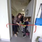 Nauczycielka wraz z dziećmi przecinająca czerwona wstęgę w drzwiach sali.